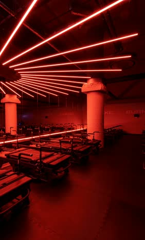 Pilates studio lit in deep red, with rows of reformers and fanned linear ceiling lights between concrete columns