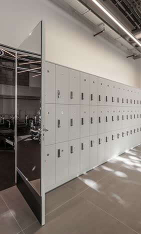 Corridor with a wall of pale grey lockers and a full-height mirror panel reflecting the studio