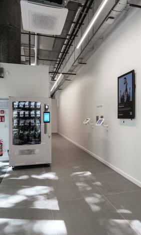 Entrance area with a vending machine, wall-mounted tablets and a digital display screen, under exposed ceiling services