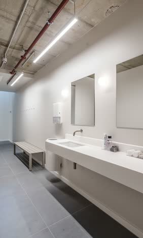 Washroom with a long white trough basin, two wall mirrors, a timber bench and exposed ceiling pipework