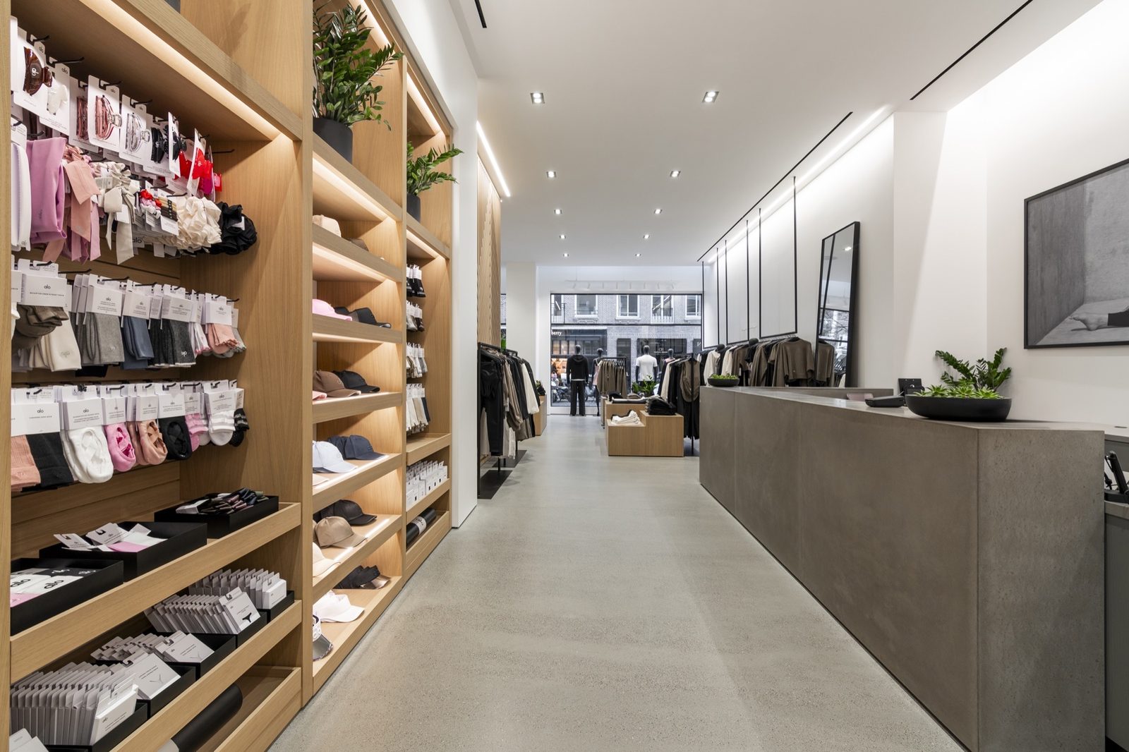 Long retail floor with oak wall shelving, a polished concrete counter and a glazed shopfront beyond