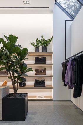 Corner of the store with a fiddle-leaf fig in a black planter and oak shelving of bags