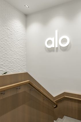 Stairwell with an illuminated brand sign on a white wall above a timber-clad balustrade