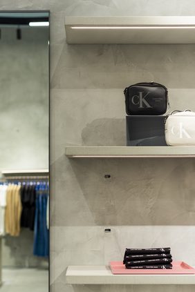 Concrete display plinths and shelving with bags, denim rails and a glazed vitrine