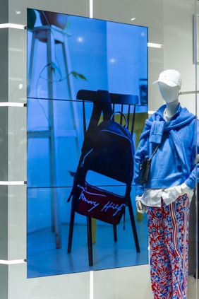 Shopfront window display with a backlit screen, a mannequin and a branded backpack on a chair