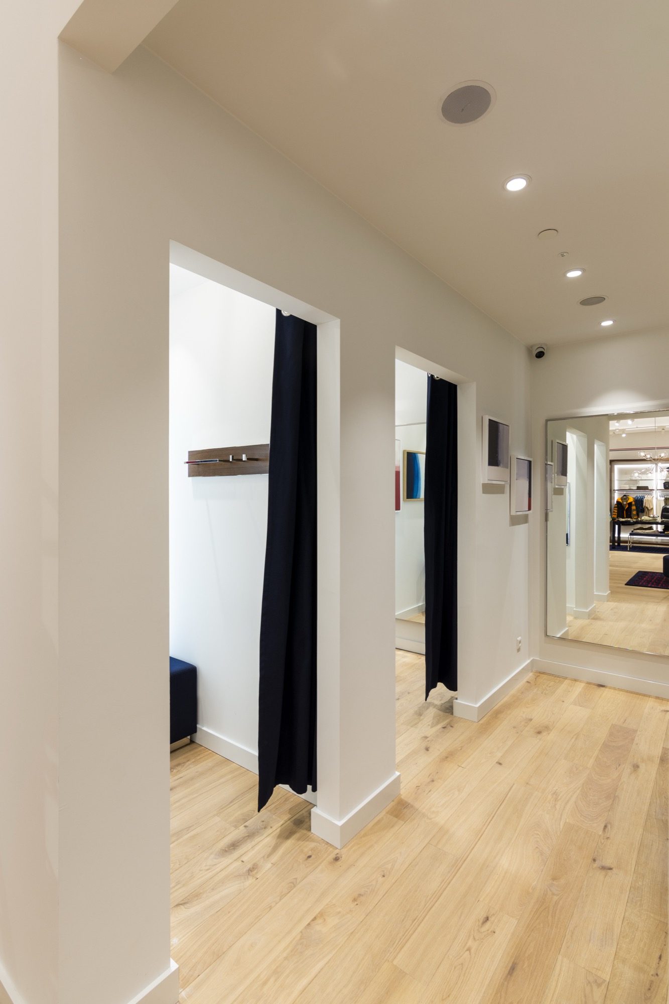 Fitting room corridor with curtained cubicles, full-height mirrors and a light oak floor