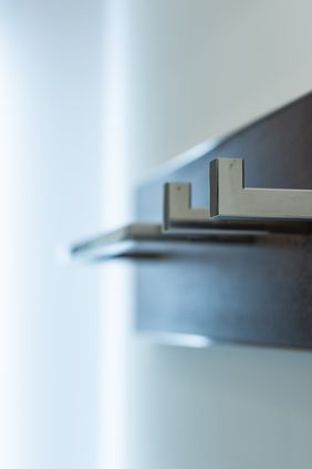Close-up of brushed-steel hanging brackets on a dark timber rail