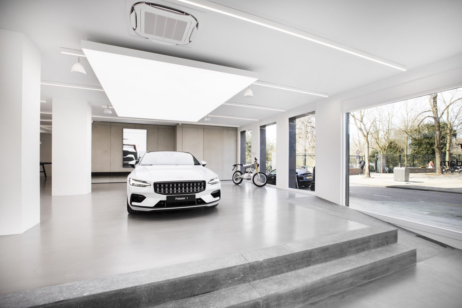 Car showroom with a white illuminated stretch ceiling, poured resin floor and full-height glazing onto the street