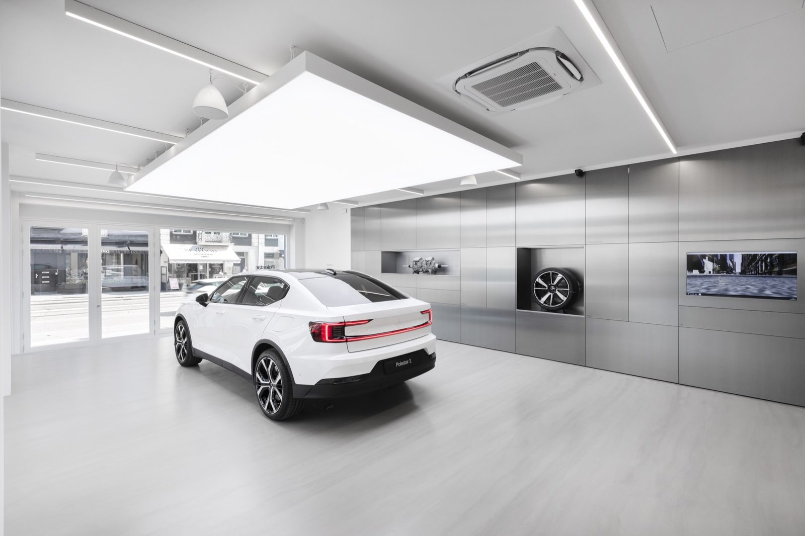 Showroom with a white car, brushed-steel wall panelling and a recessed wheel display