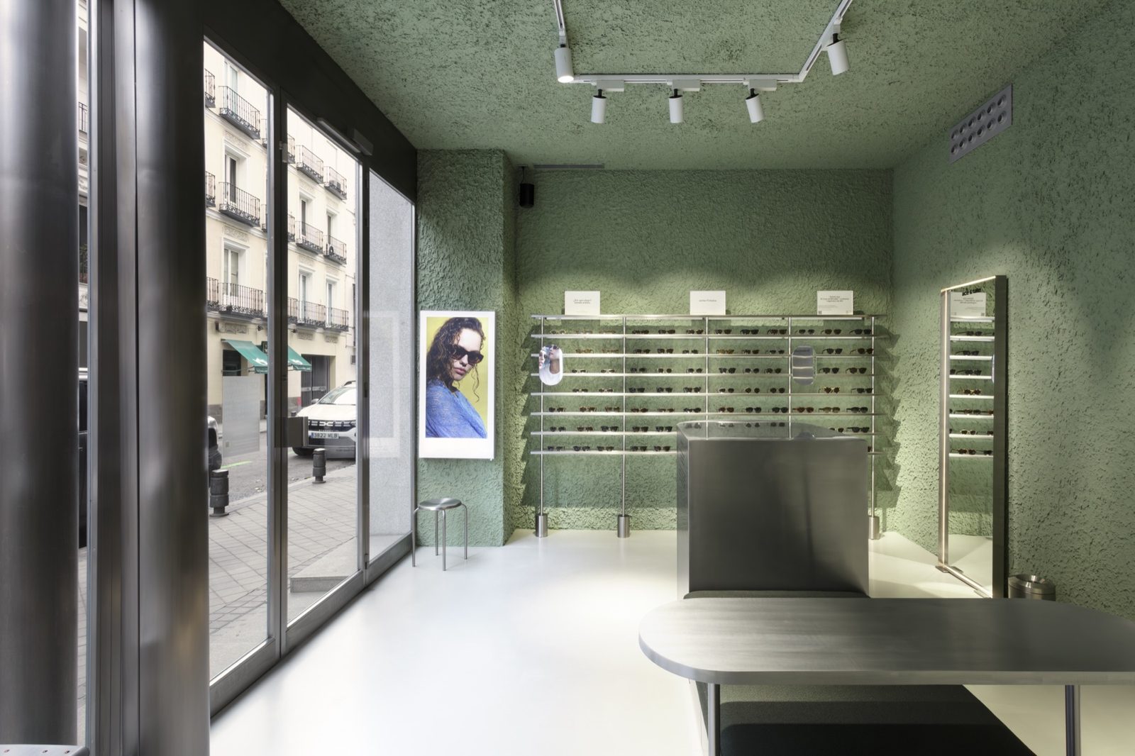 Store interior with green textured plaster walls, a glazed shopfront and wall-mounted steel display rails of eyewear