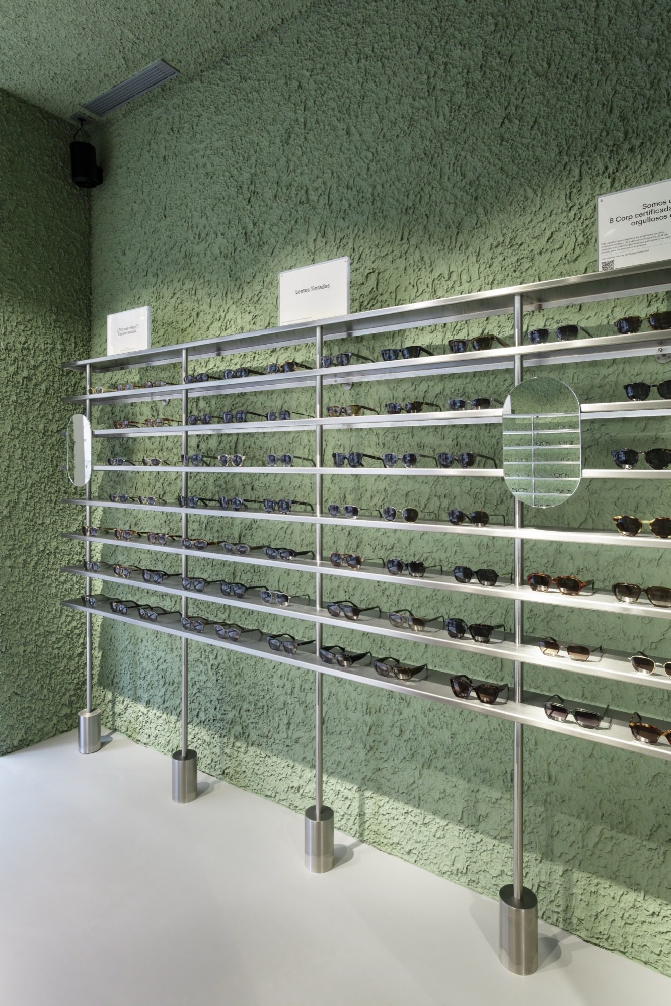 Wall of brushed-steel display rails holding eyewear against green textured plaster