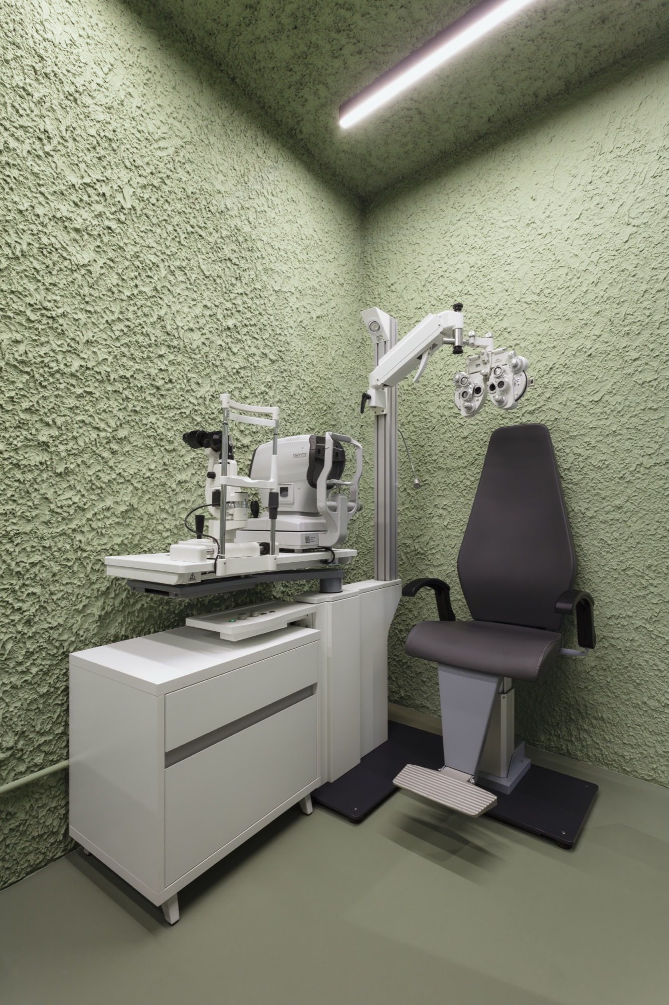 Close-up of a phoropter on its stand against a green textured plaster wall
