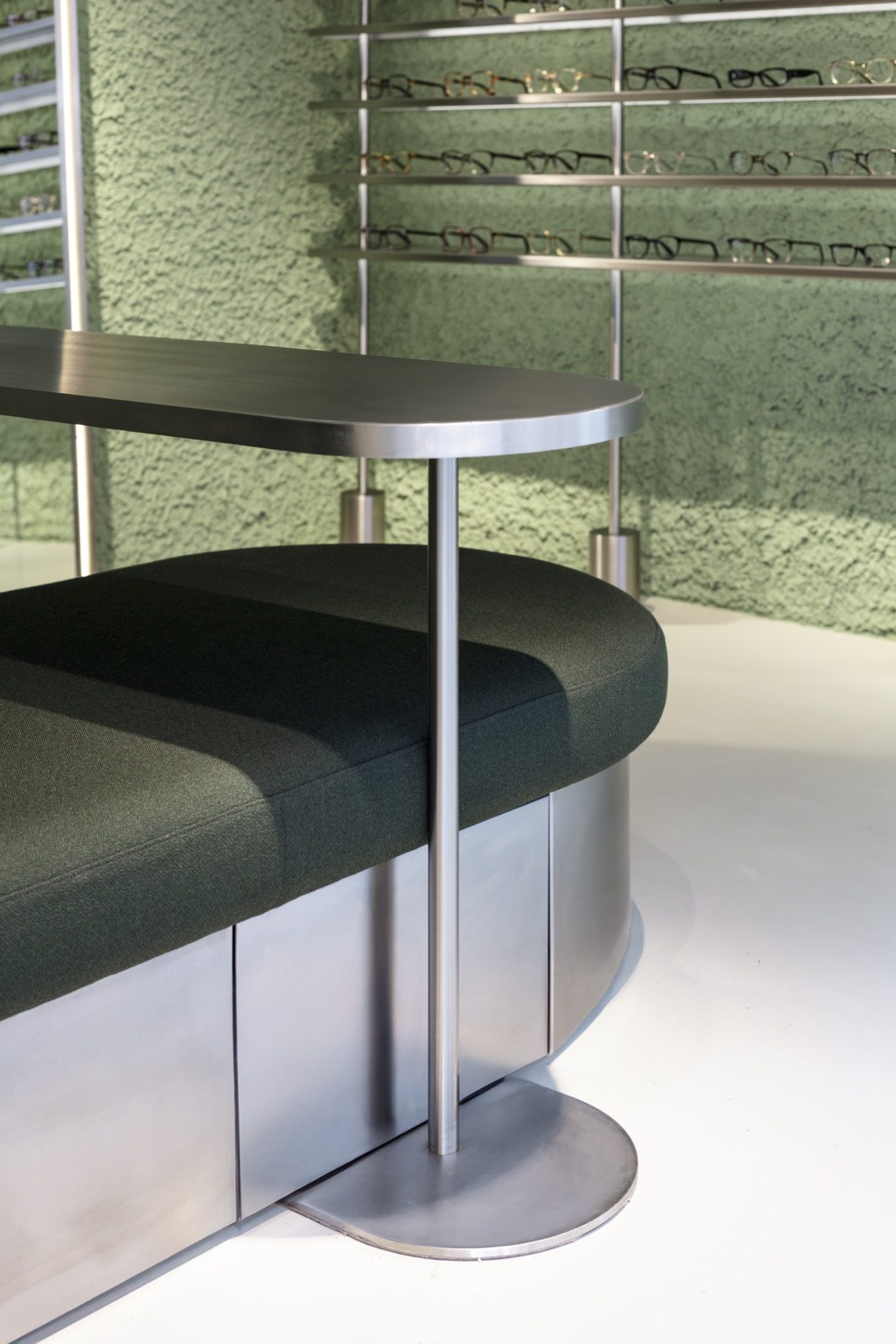 Detail of the curved steel counter and upholstered bench, with eyewear rails behind
