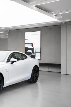 Showroom with a white car beside concrete-look wall panelling, a recessed backlit image panel and an illuminated ceiling plane